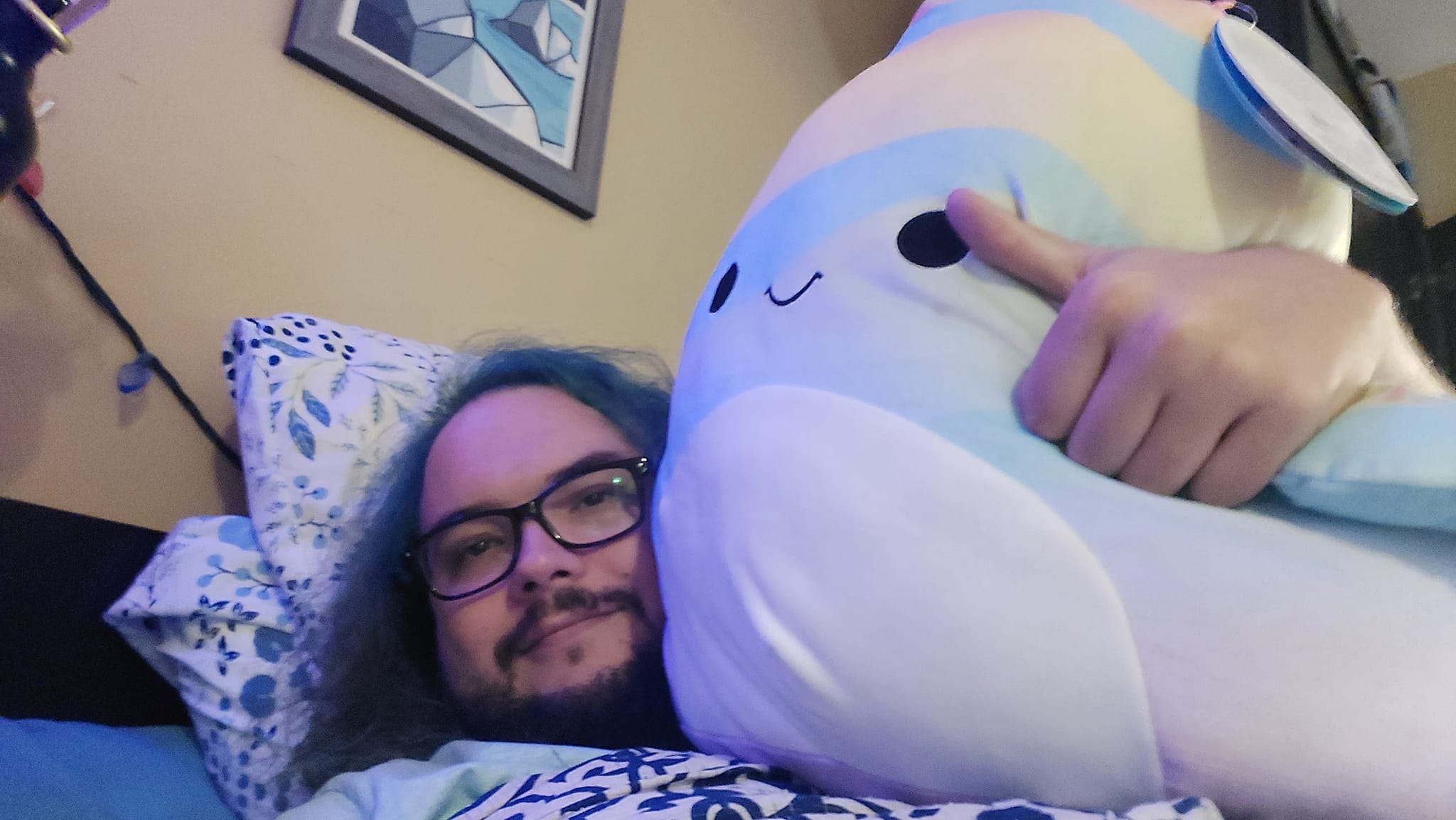 A man with green hair laying with a large Squishmallow fish, Photo 2